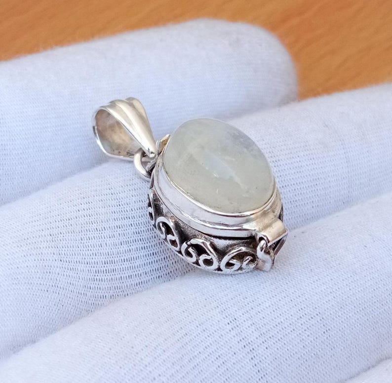 May include: A silver locket pendant with an oval-shaped white moonstone. The locket has a detailed, ornate design and a hinged opening.