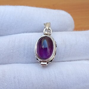 May include: A silver pendant with a purple amethyst gemstone. The pendant has a detailed design and a hinged opening.