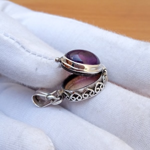 May include: A silver locket pendant with an amethyst gemstone. The locket is open, revealing a heart-shaped design on the inside.
