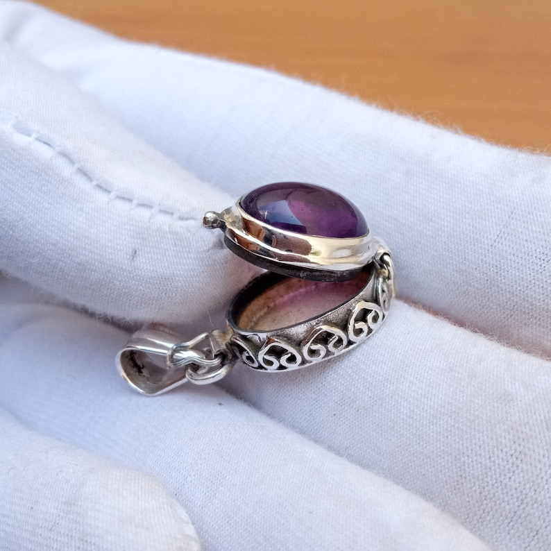 May include: A silver locket pendant with an amethyst gemstone. The locket is open, revealing a heart-shaped design on the inside.