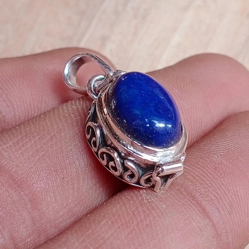 May include: A silver pendant with a blue lapis lazuli stone set in an ornate silver frame. The pendant has a bail for attaching to a chain.
