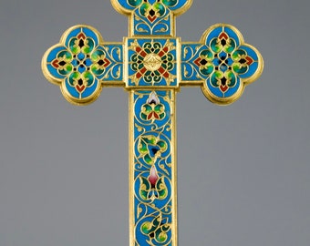 May include: A gold-colored cross with intricate enamel detailing. The cross features a blue background with floral patterns in green, red, and gold. The cross has a decorative base and is set against a gray backdrop.