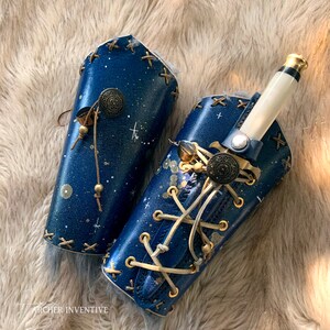 May include: Two blue leather arm cuffs with gold accents and a decorative dagger. The cuffs have a starry sky design and are tied with a white cord.
