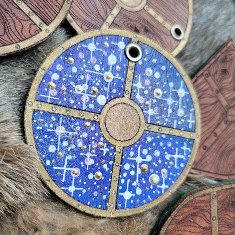 May include: A blue and gold round wooden shield with a white dot pattern. The shield has a hole in the top for hanging.