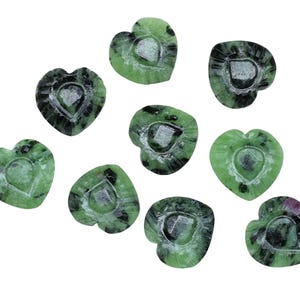 May include: A collection of heart-shaped stones in shades of green and black, each with a heart carved into it. The stones are scattered against a white background, highlighting their natural patterns and textures. These decorative stones are ideal for crafts.