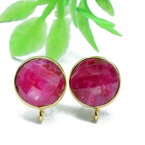 Pode incluir: Um par de brincos dourados com pedras redondas de rubi vermelho facetadas. Os brincos têm um design simples e elegante.