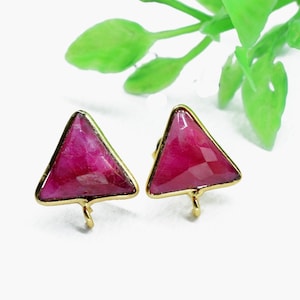 以下が含まれることがあります： 三角形の赤い宝石のアクセントが付いた、ゴールドトーンのイヤリングのペアです。