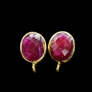 Pode incluir: Um par de brincos ovais de pedra preciosa vermelha rubi com engastes de ouro e um pequeno laço de ouro na parte inferior.
