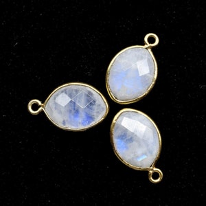 Könnte beinhalten: Drei ovale Mondstein-Anhänger mit goldfarbenen Metallfassungen. Die Steine sind durchscheinend und haben eine milchig weiße Farbe mit einem blauen, irisierenden Schimmer.