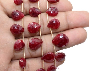 May include: A strand of deep red gemstone beads in a teardrop shape. The beads are strung on a thin gold wire.