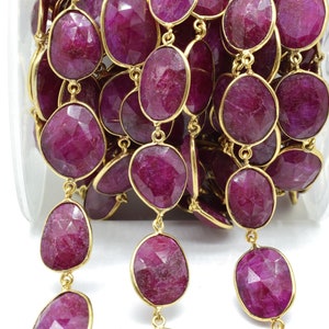 May include: A close-up of a strand of ruby gemstone beads with gold connectors. The beads are faceted and have a deep red color.