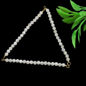 Puede incluir: Un collar de cuentas blancas con cierres dorados, formando una forma triangular.