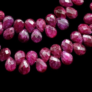 May include: A strand of deep red ruby gemstone beads, each bead is faceted and shaped like a teardrop. The beads are strung together in a double row, creating a beautiful and elegant necklace.