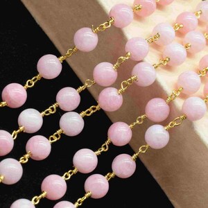 May include: Multiple strands of pink gemstone beads linked by gold-coloured chains. The beads are a soft pink hue and spherical. The arrangement in parallel rows suggests they are for jewellery making, perhaps necklaces or bracelets.