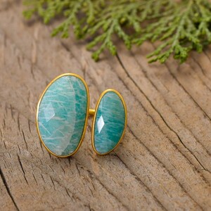 Puede incluir: Un anillo de oro con dos piedras preciosas verdes de forma ovalada. El anillo está colocado sobre una superficie de madera.