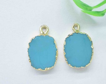 May include: Two gold-rimmed oval-shaped pendants with a light blue glass center. The pendants are on a white background.