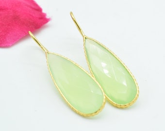 Puede incluir: Un par de pendientes en forma de lágrima con una piedra preciosa verde claro engastada en un marco de metal dorado.