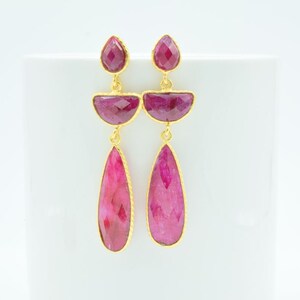Può includere: Un paio di orecchini d'oro con gocce di pietre preziose rosa. Gli orecchini presentano tre pietre preziose rosa su ogni orecchino, con la pietra preziosa inferiore a forma di lacrima.