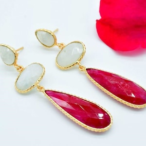 Op de afbeelding: Gouden oorbellen met twee witte ovale stenen en een traanvormige rode steen.