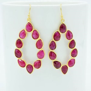 May include: Gold hoop earrings with a teardrop shape, featuring a cluster of pink gemstones.