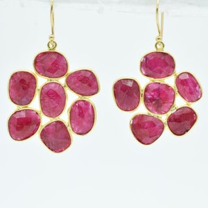May include: A pair of gold earrings featuring a cluster of pink ruby stones. The earrings are designed in a flower shape.