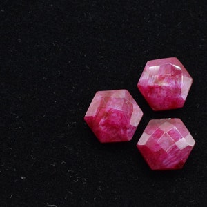 May include: Three pink faceted gemstone cabochons in a hexagonal shape on a black background.