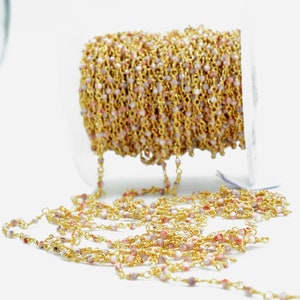 May include: A spool of gold chain with pink and white beads. The chain is made of small, delicate links and is ideal for making jewellery.