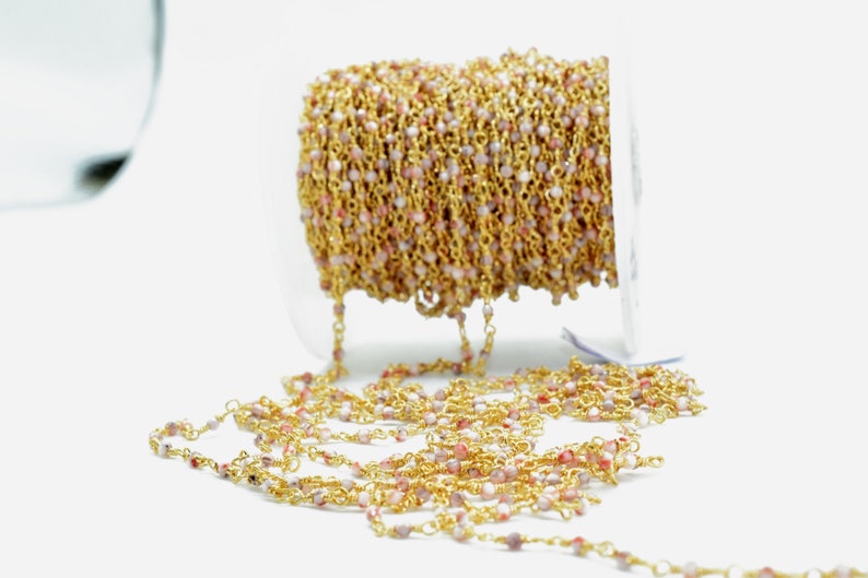 May include: A spool of gold chain with pink and white beads. The chain is made of small, delicate links and is ideal for making jewellery.