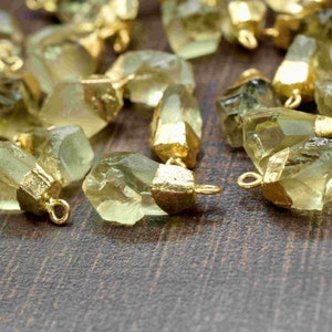 May include: A collection of green gemstone pendants with gold-plated accents. The pendants are faceted and have a natural, raw look. They are perfect for jewellery making or crafting.