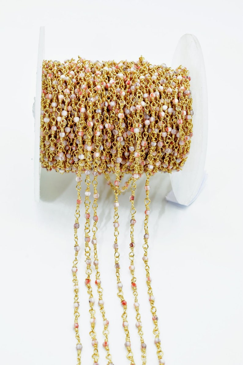 May include: A spool of gold-toned chain with small, pink and white beads. The chain is made of metal and the beads are made of stone.