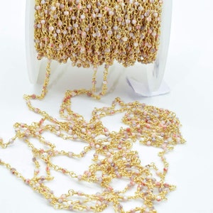 May include: A spool of gold chain with pink and white beads. The chain is made of small, round beads that are strung together with a gold wire. The chain is approximately 46 cm long and is ideal for jewellery making.