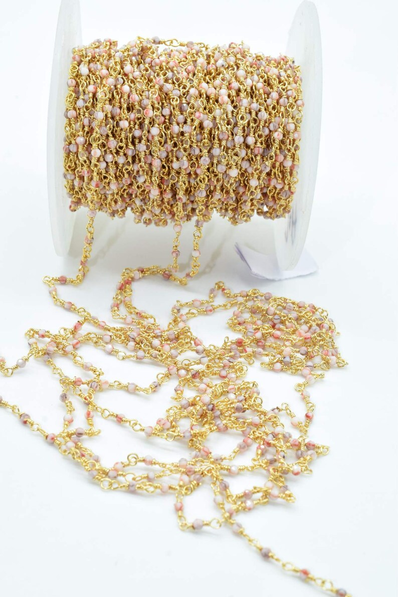 May include: A spool of gold chain with pink and white beads. The chain is made of small, round beads that are strung together with a gold wire. The chain is approximately 46 cm long and is ideal for jewellery making.