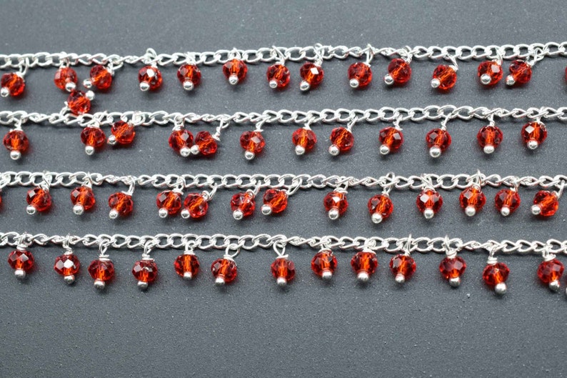 K&ouml;nnte beinhalten: Eine silberne Kette mit mehreren Reihen von baumelnden roten Glasperlen.