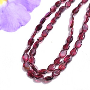 May include: A strand of oval-shaped, faceted, red garnet beads. The beads are strung on a clear thread and are approximately 6mm in size.