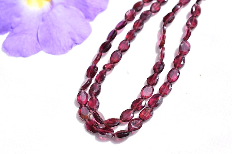 May include: A strand of oval-shaped, faceted, red garnet beads. The beads are strung on a clear thread and are approximately 6mm in size.