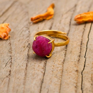 May include: A gold ring featuring a large, faceted, pink gemstone set in a claw setting.