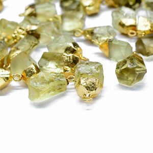 May include: A collection of raw, light green gemstone pendants with gold-toned metal accents. The pendants are irregularly shaped and have a natural, rough texture.