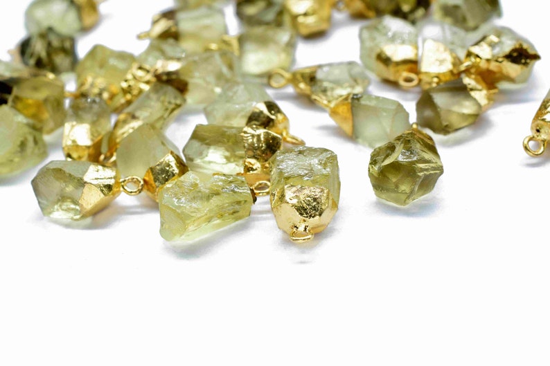 May include: A collection of raw, light green gemstone pendants with gold-toned metal accents. The pendants are irregularly shaped and have a natural, rough texture.