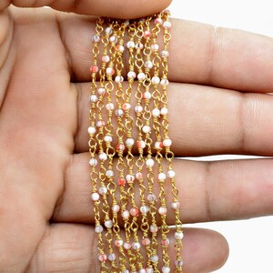 May include: A gold chain with small white and pink beads. The chain is laid out in a straight line on a hand.