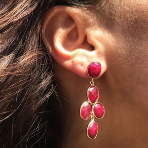 May include: Gold dangle earrings with a cluster of five red gemstone drops.