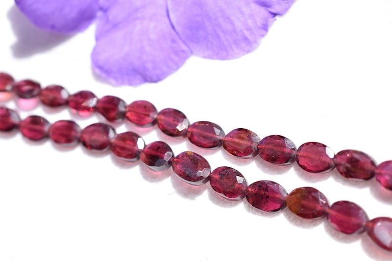 May include: A strand of oval-shaped, faceted, dark red gemstone beads. The beads are strung on a clear thread and are arranged in a double row.