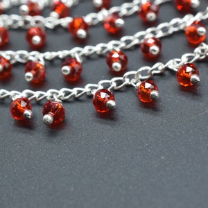 K&ouml;nnte beinhalten: Eine silberne Kettenkette mit mehreren Str&auml;ngen und roten Kristallperlen. Die Perlen h&auml;ngen an der Kette und sind facettiert.