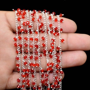 K&ouml;nnte beinhalten: Eine silberne Kette mit roten Glasperlen, die daran h&auml;ngen. Die Kette liegt auf einer Hand.