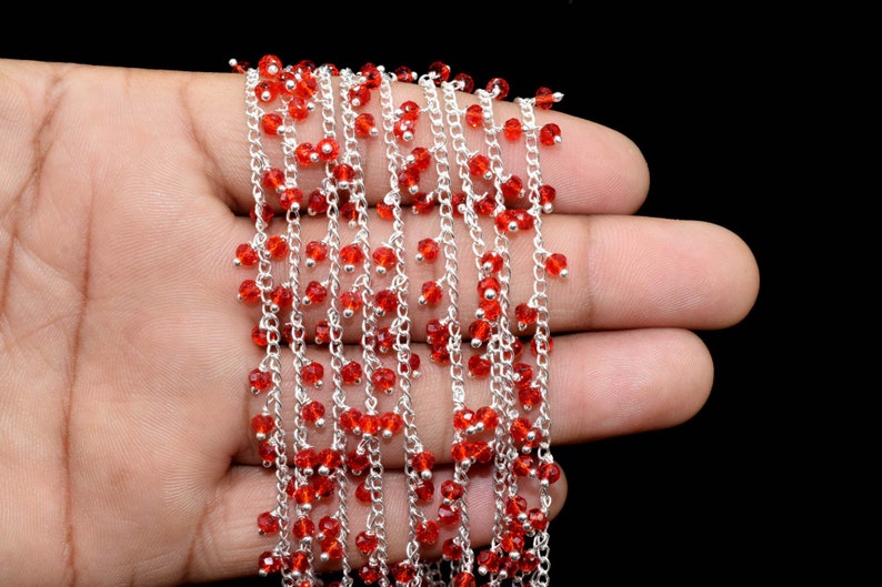 K&ouml;nnte beinhalten: Eine silberne Kette mit roten Glasperlen, die daran h&auml;ngen. Die Kette liegt auf einer Hand.