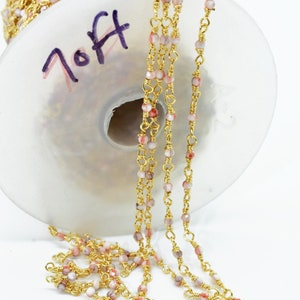May include: Gold chain with pink and white beads. The chain is wound around a spool with the word "7 Off" written on it.