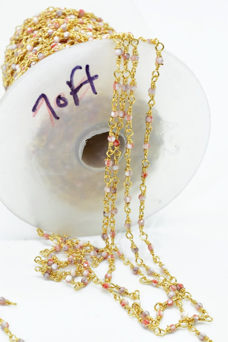 May include: Gold chain with pink and white beads. The chain is wound around a spool with the word "7 Off" written on it.