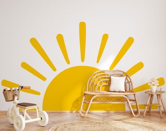 May include: A yellow sun wall decal with a half-circle and radiating lines is the focal point of this room. A small white tricycle with a wicker basket, a woven bench, and a round jute rug complete the decor. The sun decal is 81 inches x 44.5 inches.