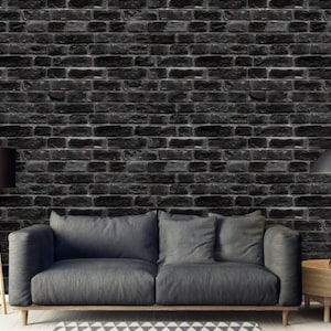 May include: A dark grey brick wall with a grey sofa and two lamps in front of it. The sofa has two cushions and a side table with a lamp on it.