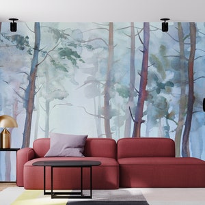 Op de afbeelding: Een rode bank met een grijs kussen staat voor een aquarelmuurschildering die een mistig bos met hoge bomen voorstelt. De kamer is ingericht met een gouden lamp en een zwarte staande lamp.