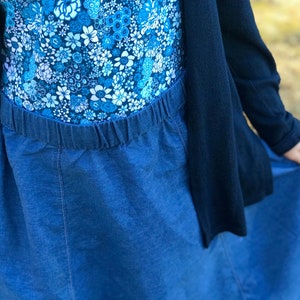 May include: A blue denim skirt with an elastic waistband. The skirt is long and flowing, and it is paired with a floral print top.